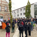 Mehrere Dutzend Menschen stehen bei einer Demonstration in einem Halbkreis.