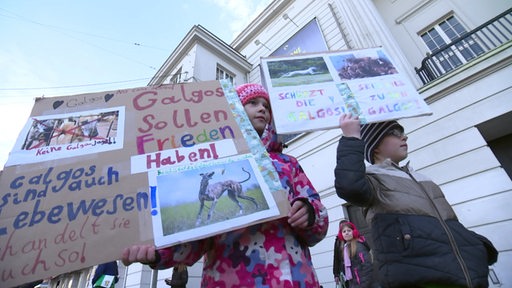 Zwei Kinder die Pappschilder mit der Aufschrift "Galogos sollen Frieden haben" hochhalten.