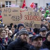 Mehrere Menschen halten bei einer Kundgebung bemalte Plakate in die Höhe.