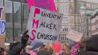 Ein Schild wird bei einer Demonstration in die Höhe gehalten.