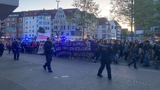 Menschen laufen während einer Demonstration über eine Straße in der Bremer Neustadt. Im Vordergrund sind Polizisten zu sehen.
