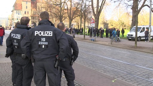 Drei Polizisten stehen mit dem Rücken zur Kamera und beobachten in Uniform den Verlauf der Demo. 