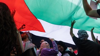 Menschen stehen unter einer riesigen Palästina-Flagge und jubeln