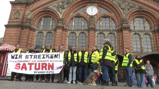 Streikende Personen in gelben Verdi-Westen und mit Banner vor dem Bremer Hauptbahnhof.