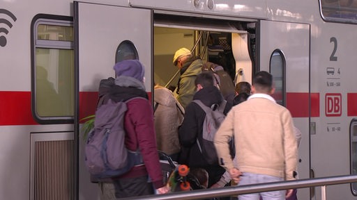 Mehrere Personen steigen in einen Zug am Bahnhof ein.