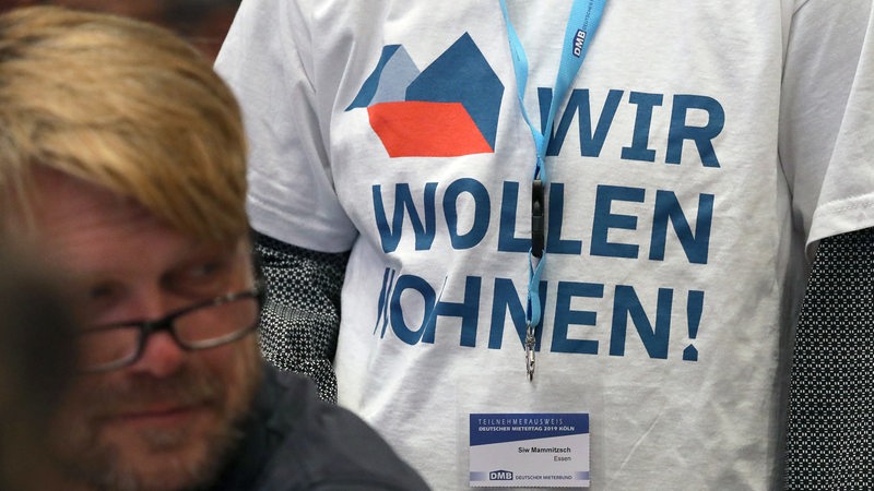Eine Teilnehmerin der Versammlung steht mit einem T-Shirt mit der Aufschrift "Wir wollen Wohnen" auf der Jahrestagung des Deutschen Mieterbundes im Plenum.