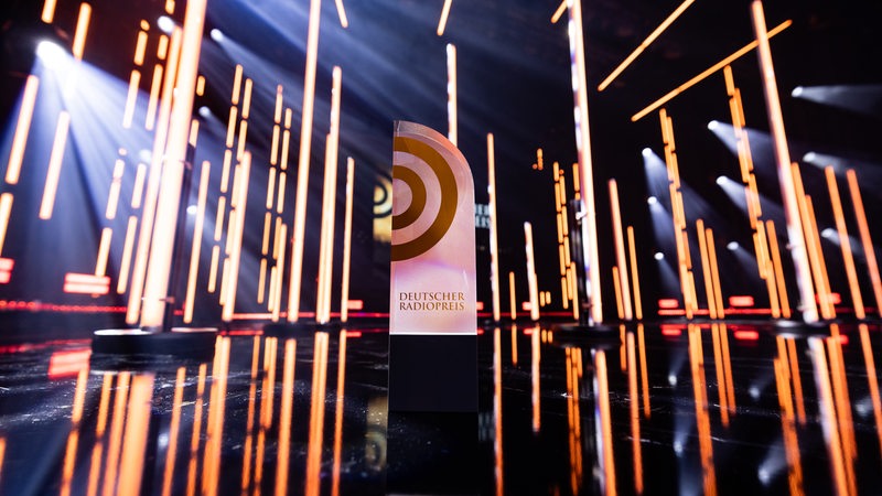 Auf einer Bühne steht eine Trophäe mit der Aufschrift "Deutscher Radiopreis".