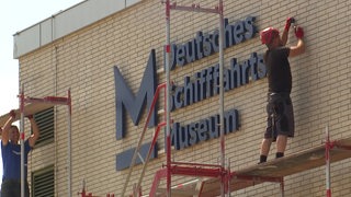Der Schriftzug des Deutschen Schifffahrtsmuseums vor dem ein Baugerüst mit Arbeitern steht.