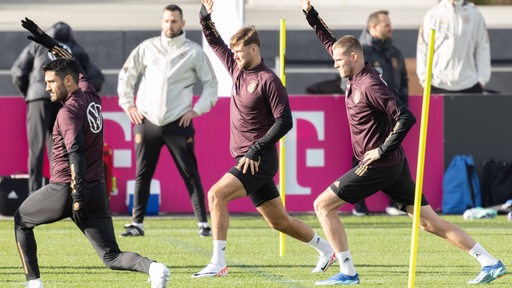 Die DFB-Spieler Ilkay Gündogan, Niclas Füllkrug und Marvin Ducksch dehnen sich und strecken ihre rechten Arme in die Höhe.