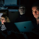 Szene aus "Die Welt zwischen den Nachrichten": Menschen sitzten im Dunkeln vor ihren Laptops
