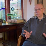 Ein Mann sitzt auf einem Stuhl und gestikuliert.