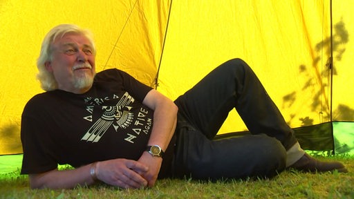 Dirk Thiele liegt auf dem Boden im Gras unter einem gelben Tipi.