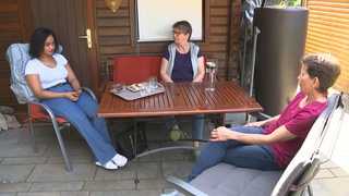 Drei Frauen sitzen zusammen auf einer Terrasse.