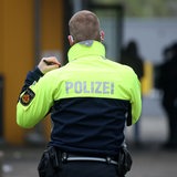 Rückenansicht eines Polizisten mit Warnweste vor einer Schule