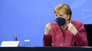Bundeskanzlerin Merkel nimmt sich eine Schutzmaske ab.