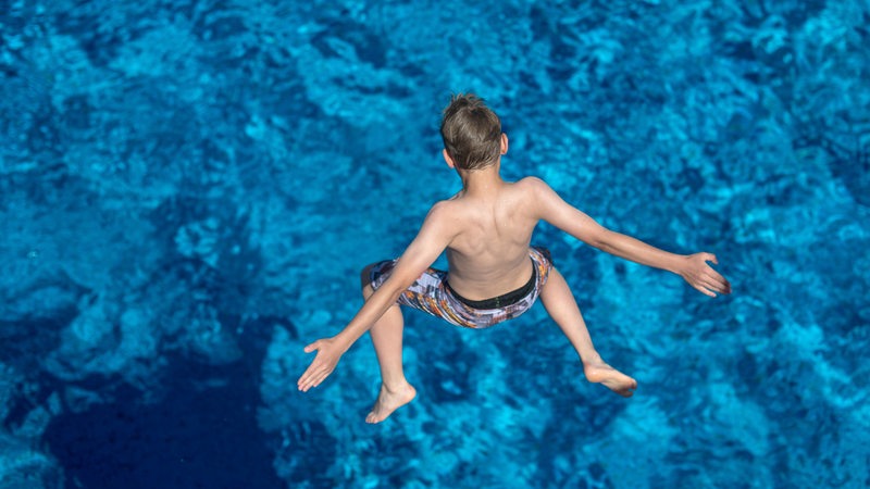 Ein Junge springt von einem Sprungturm in ein Schwimmbecken.