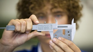 Ein Auszubildender zum Industriemechaniker prüft mittels einer Schieblehre das Maß des von ihm angefertigten Werkstücks.
