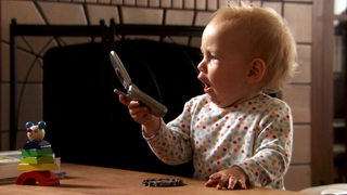 Ein Baby hat ein Handy in der Hand.