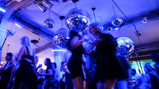 Dutzende Menschen tanzen zur Musik auf einer Tanzfläche in einem Club.