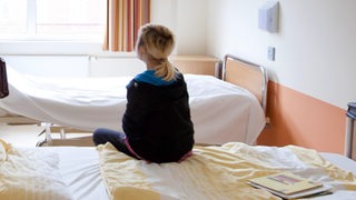 Ein Mädchen sitzt auf einem Krankenhausbett in einer psychiatrischen Klinik (Archivbild)