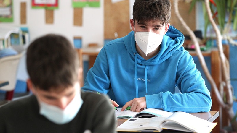 Zwei Schüler sitzen mit Masken in einem Klassenraum.