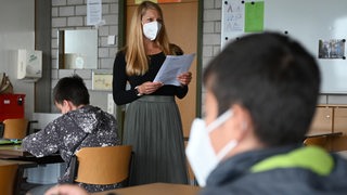 Eine Lehrerin steht in einem Klassenzimmer.