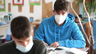 Zwei Schüler sitzen mit Masken in einem Klassenzimmer.