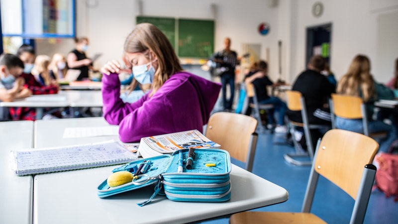 Ein Mädchen sitzt mit Maske in einem Unterrichtsraum.