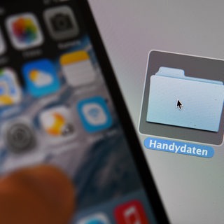 Ein Handydisplay, im Hintergrund ein Computer-Desktop.