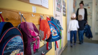 In einer Kindertagesstätte sind mehre Rucksäcke auf Haken aufgehängt.