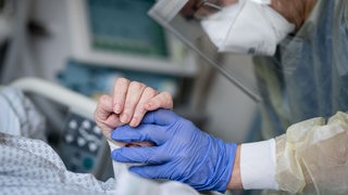 Eine Pflegeperson hält die Hand eines Corona-Patienten