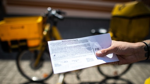 Postbote hält Wahlbenachrichtigung zur Bundestagswahl 2021 in der Hand.