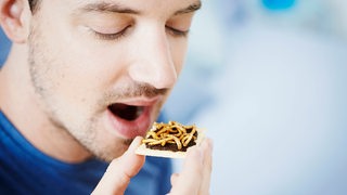 Ein Mann führt ein Stück Brot mit Würmern darauf zum Mund.