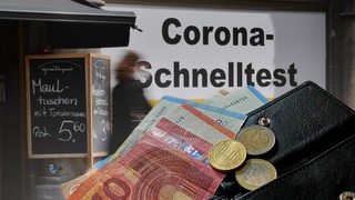 Fotomontage: Geldscheine im Vordergrund, im Hintergrund ein Plakat mit der Aufschrift "Corona Schnellstest"