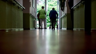Eine Pflegefachkraft geht mit Bewohnern durch ein Seniorenheim 