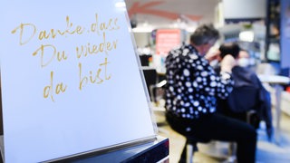 Ein Schild "Du bist wunderschön. Danke, dass Du wieder da bist" steht auf dem Empfangstresen im Friseursalon von Holger Knievel. 