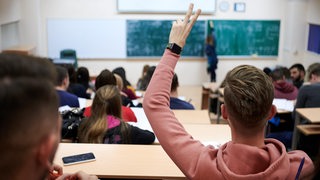 Ein  junger Mann in einem Hörsaal hebt die Hand