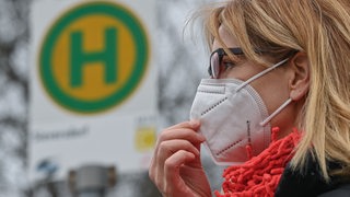 Eine Frau trägt eine Schutzmaske an einer Bus-Haltestelle.