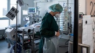 Eine Mitarbeiterin der Pflege steht in einem Patientenzimmer einer Corona-Intensivstation.