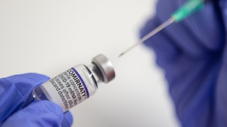 Eine Impfnadel sticht in eine Ampulle mit Impfstoff.