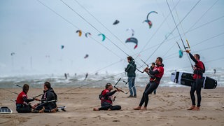 Kiter stehen an einem Strand und halten ihre Kites fest.
