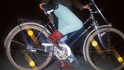 Das Nachtbild zeigt die Reflektoren an einem Fahrrad, auf das eine Frau aufsteigt