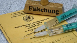 Auf einem Impfausweis befinden sich zwei Spritzen und ein Stempel mit dem Schriftzug Faelschung.