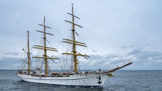 Ein Segelschiff mit drei Masten fährt auf offenem Wasser.