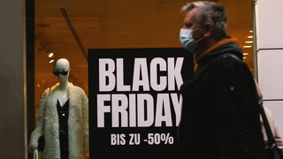 Ein Mann mit Schutzmaske läuft an einem Schaufenster mit der Aufschrift "Black Friday" vorbei