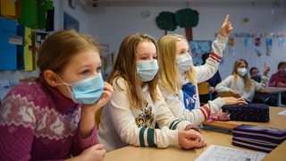 Mehrere Kinder sitzen mit Masken in einem Klassenraum.