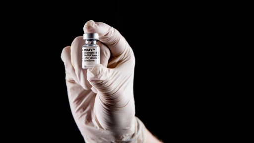 Eine Person mit Schutzhandschuhen hat eine Impfampulle mit dem mRNA-Impfstoff Comirnaty, BNT162b2, Biontech / Pfizer