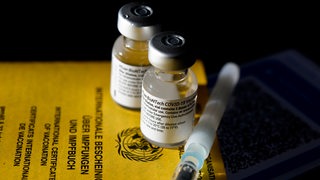 Auf einem gelben Impfpass liegen zwei Impfdosen und eine Spritze.