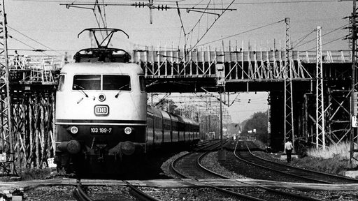 Eine Elektrolok E03 103 189-7 der Deutschen Bundesbahn fährt am 24.05.1979 in Diepholz in Niedersachsen an einer Baustelle für einen neuen Bahnübergang vorbei.