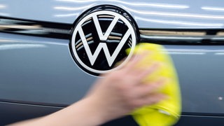 Ein Mitarbeiter von Volkswagen streicht im Rahmen eines Presserundgangs im Lichttunnel in der Gläsernen Manufaktur von Volkswagen mit einem Tuch über einen VW ID.3.